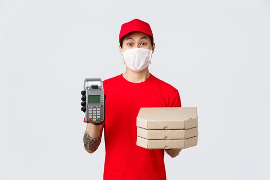 Contactless delivery, safe purchase, shopping during coronavirus concept. Enthusiastic pizza delivery guy in medical mask and gloves, bring order to client paying with credit card using POS terminal.