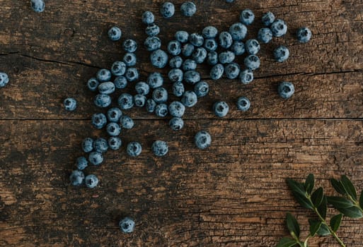 Blue fresh blueberries are scattered on an old brown wooden cracked table.