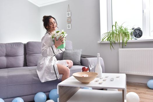 Beautiful brunette woman dressing gown with bouquet indoors. Female portrait in living room