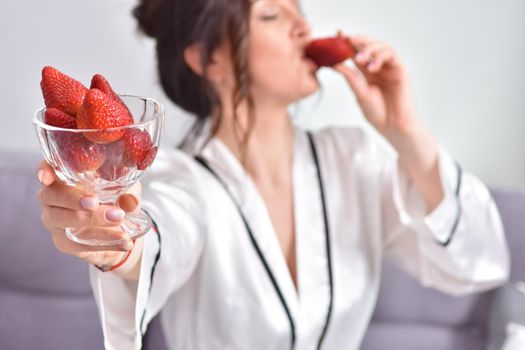 Portrait of happy young brunette woman holding bowl of juicy red strawberries