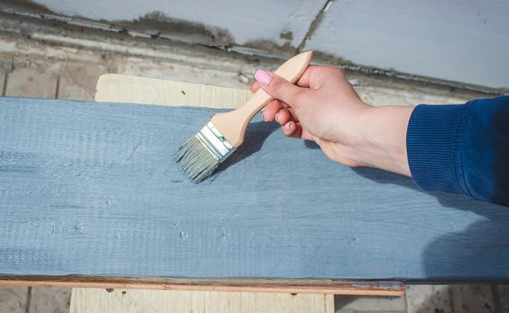 girl paints a board with a brush. Paint with gray paint. selective focus