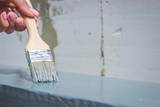 girl paints a board with a brush. Paint with gray paint. selective focus