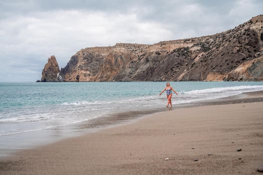 A plump woman in a bathing suit enters the water during the surf. Alone on the beach, Gray sky in the clouds, swimming in winter