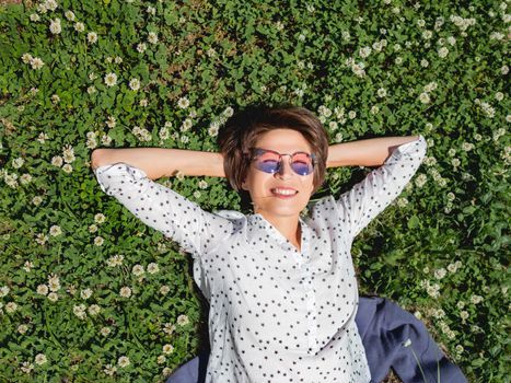 Top view on woman lying among clover flowers on lawn in urban park. Nature in town. Relax outdoors after work. Summer vibes.