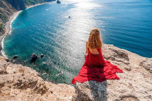 A girl with flowing hair in a long red dress sits on a rock above the sea. The stone can be seen in the sea