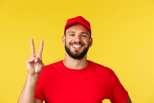 Close-up friendly cheerful, bearded delivery guy show peace sign, wear red uniform cap and t-shirt, courier likes taking care customer orders, safely shopping and parcel transfer, yellow background.