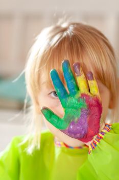 Little girl hiding behing her watercolour painted hand at home during the pandemic lockdown.