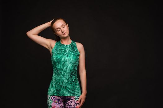 Front view of strong red haired woman in green uniform looking at camera and posing on black isolated background. Muscular girl keeping fit and training. Concept of health and workout.