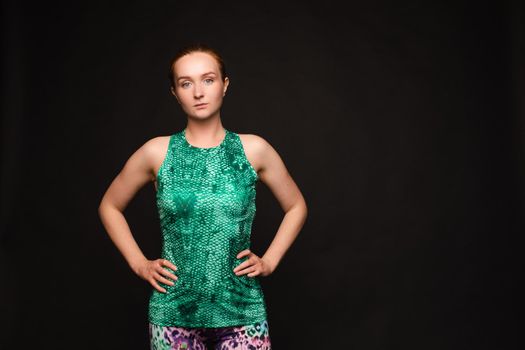 Front view of strong red haired woman in green uniform looking at camera and posing on black isolated background. Muscular girl keeping fit and training. Concept of health and workout.