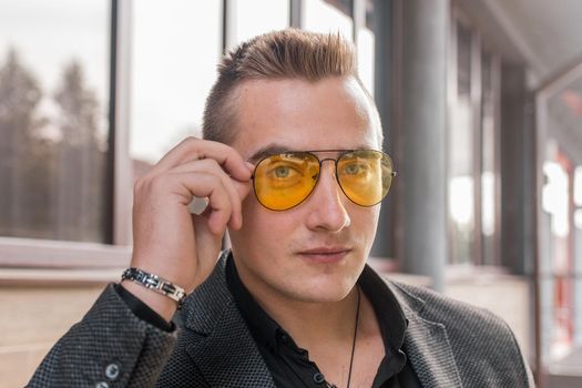 Portrait of a handsome man of European appearance businessman adjusting sunglasses with his hand, close-up on the outdoor of the street.