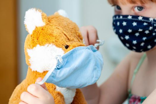 Young girl training to use a face mask during the pandemic -Focus on the teddy.