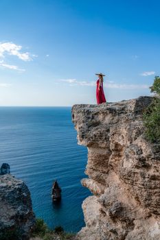 A woman in a red flying dress fluttering in the wind, against the backdrop of the sea