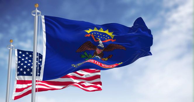 The North Dakota state flag waving along with the national flag of the United States of America. In the background there is a clear sky. North Dakota is a U.S. state in the Upper Midwest