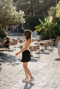 Girl tourist walking through ancient narrow street on a beautiful summer day in MEDITERRANEAN MEDIEVAL CITY , OLD TOWN bUDVA, MONTENEGRO. Young beautiful cheerful woman walking on old street at tropical town. Pretty girl looking at you and smiling