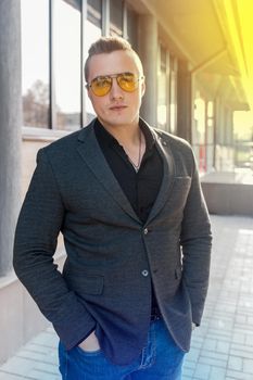 Stylish young attractive guy of European appearance businessman portrait in jacket, shirt and jeans, in sunglasses on the street outdoor.