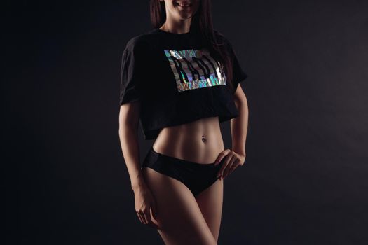 Sexy slim model in top, cap and sneakers posing and looking at camera on black isolated background in studio. Attractive woman doing sport and fitness, caring body shape. Concept of power and fit.