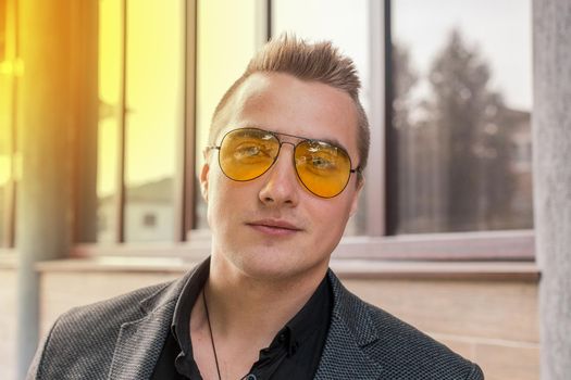 Portrait of attractive businessman of Caucasian appearance in sunglasses and jacket on street outdoor.