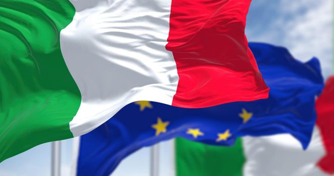 Detail of the national flag of Italy waving in the wind with blurred european union flag in the background on a clear day. Democracy and politics. European country. Selective focus.