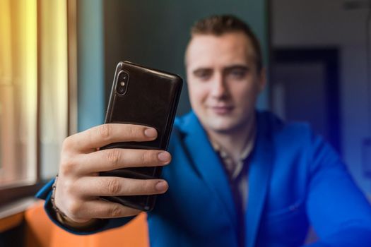 Close-up, businessman guy holds a black smartphone or mobile phone in his hand and takes a selfie or talks on a video link in a cafe.