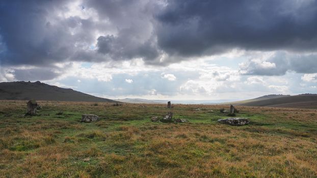 Ancient stone circle under Great Mis Tor and Great Staple Tor with dark cloudy sky overhead, Dartmoor National Park, Devon, UK