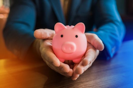 The hand of a businessman holds a pig piggy bank for storing and saving money and finances.