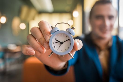 The hand of a smiling businessman man holds the alarm clock. The Concept of Time.