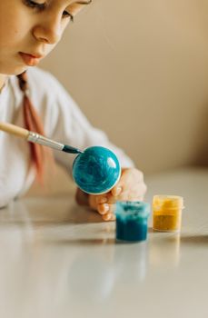 Ukrainian girl paints the egg blue and yellow. The child loves and supports his country. Cute little child girl painting with blue and yellow colors Easter eggs. Hands of a girl with a easter egg. Close-up.