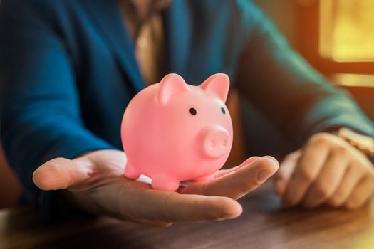 The hand of a businessman holds a pig piggy bank for storing and saving money and finances.