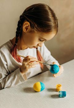 Portrait in profile of a Ukrainian girl. The child paints the egg blue and yellow. The child loves and supports his country. Cute little child girl painting with blue and yellow colors Easter eggs. Hands of a girl with a easter egg. Close-up.