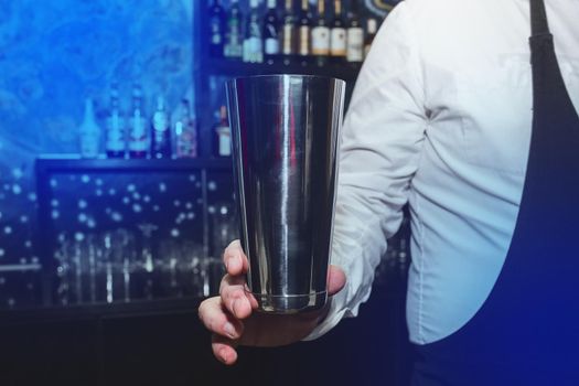 The hand of a professional bartender man holds a tool for mixing and making shaker cocktails.