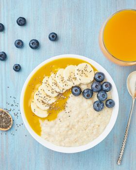 Oatmeal with bananas, blueberries, chia seeds, jam on blue wooden background. Vertical. Healthy breakfast