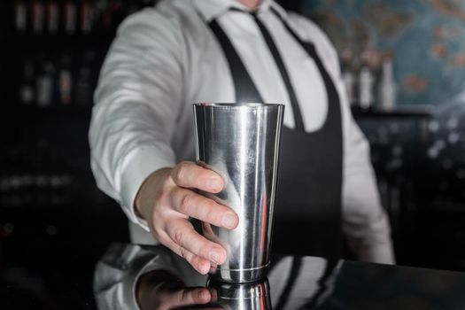 The hand of a professional bartender takes a tool for cooking and mixing alcoholic cocktail shaker, close-up.