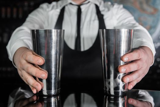 Hands of a professional bartender hold 2 tools for mixing and preparing alcoholic cocktail shakers, close-up.