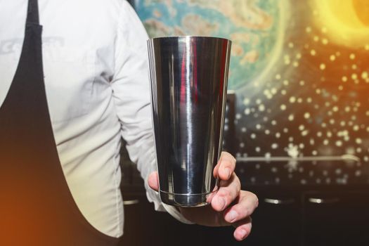 The hand of a professional bartender man holds a tool for mixing and making shaker cocktails.