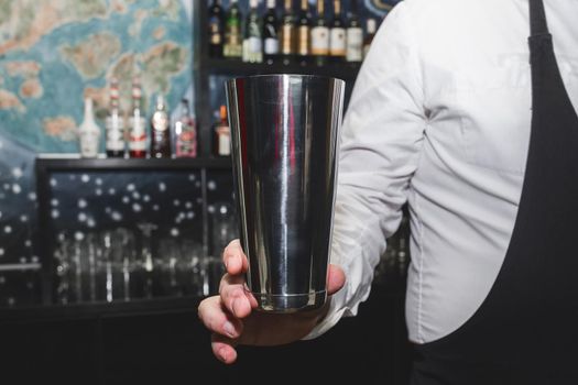 The hand of a professional bartender man holds a tool for mixing and making shaker cocktails.