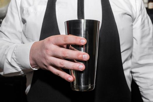 The hand of a professional bartender man holds a tool for mixing and making shaker cocktails.