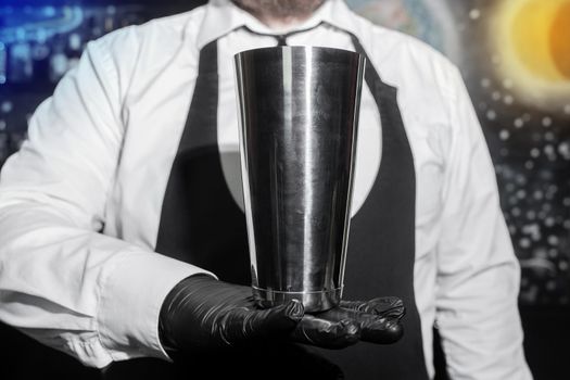 The hand of a professional bartender in a black latex glove with a bar instrument for mixing and preparing alcoholic cocktails with a shaker.