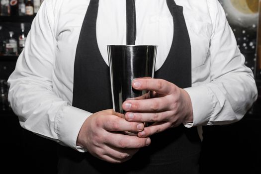 The hands of a professional bartender man holds a tool for mixing and making shaker cocktails.