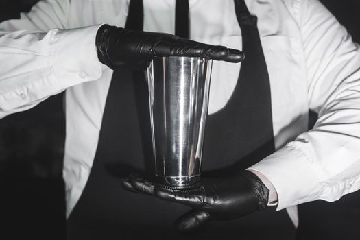 Hands of a professional bartender in latex rubber gloves hold a tool for preparing and mixing alcoholic cocktail shaker, close-up.