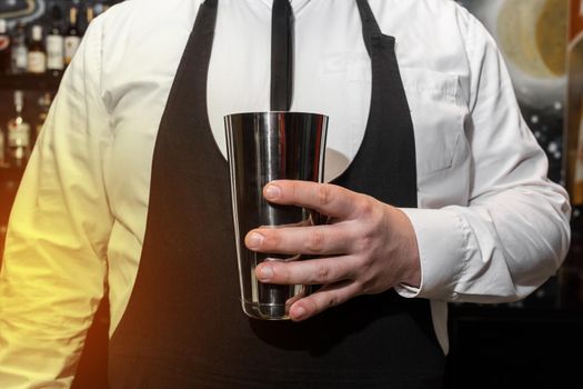 The hand of a professional bartender man holds a tool for mixing and making shaker cocktails.