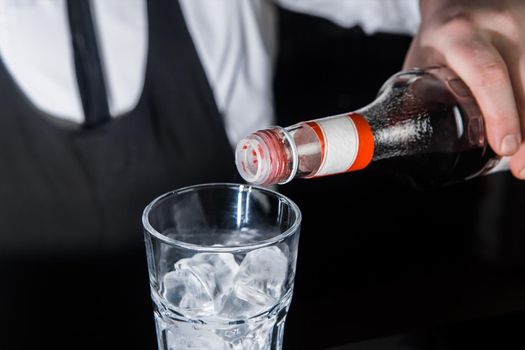 The hand of a professional bartender pours red syrup into a glass of ice cubes. The process of preparing an alcoholic cocktail.