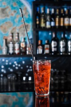 Red alcoholic chilled cocktail drink in glass with bar spoon on the bar counter of the nightclub.