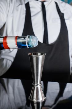 The hand of a professional bartender pours blue syrup into a tool to control the ingredients added to a jigger cocktail or measuring cup. The process of preparing a cocktail.