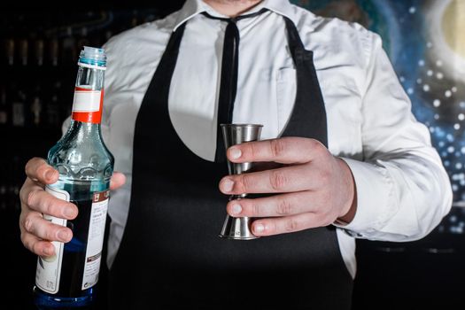 The hand of a professional bartender pours blue syrup into a tool to control the ingredients added to a jigger cocktail or measuring cup. The process of preparing a cocktail.