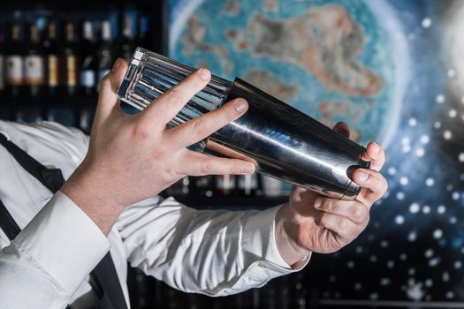 Hands of a professional bartender beat and mix ingredients in a tool for making alcoholic cocktails with a metal shaker.