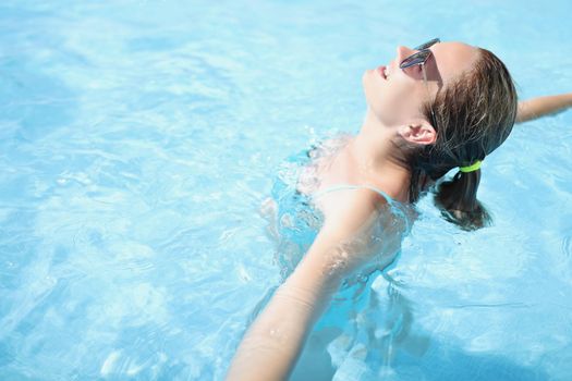 Portrait of happy young woman swim in pool, enjoy sun, sunbathe in water, relaxing atmosphere on vacation, sunny day. Holiday, resort, hotel, fun concept