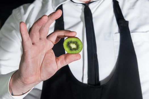 The hand of a professional bartender holds a cut piece of kiwi citrus, close-up.