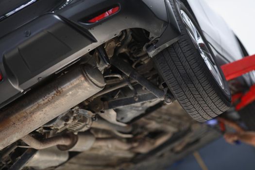 Close-up of car lifted in maintenance service for checkup, undercarriage of automobile, bottom view of elevated machine. Pit stop, car diagnostic concept
