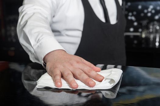 The hand of a professional bartender wipes the bar counter with a napkin or cloth, cleans and prepares the workplace.