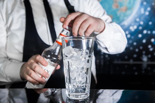 The process of preparing a cocktail. Professional bartender with a bottle of syrup in his hands next to a glass of ice cubes on the bar counter.